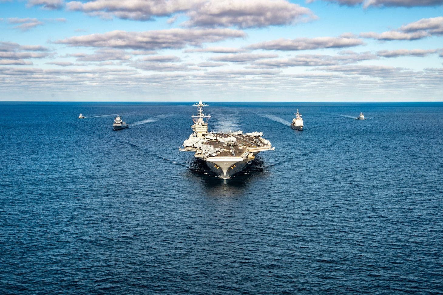 Wide shot of aircraft carrier with escort ships in the ocean
